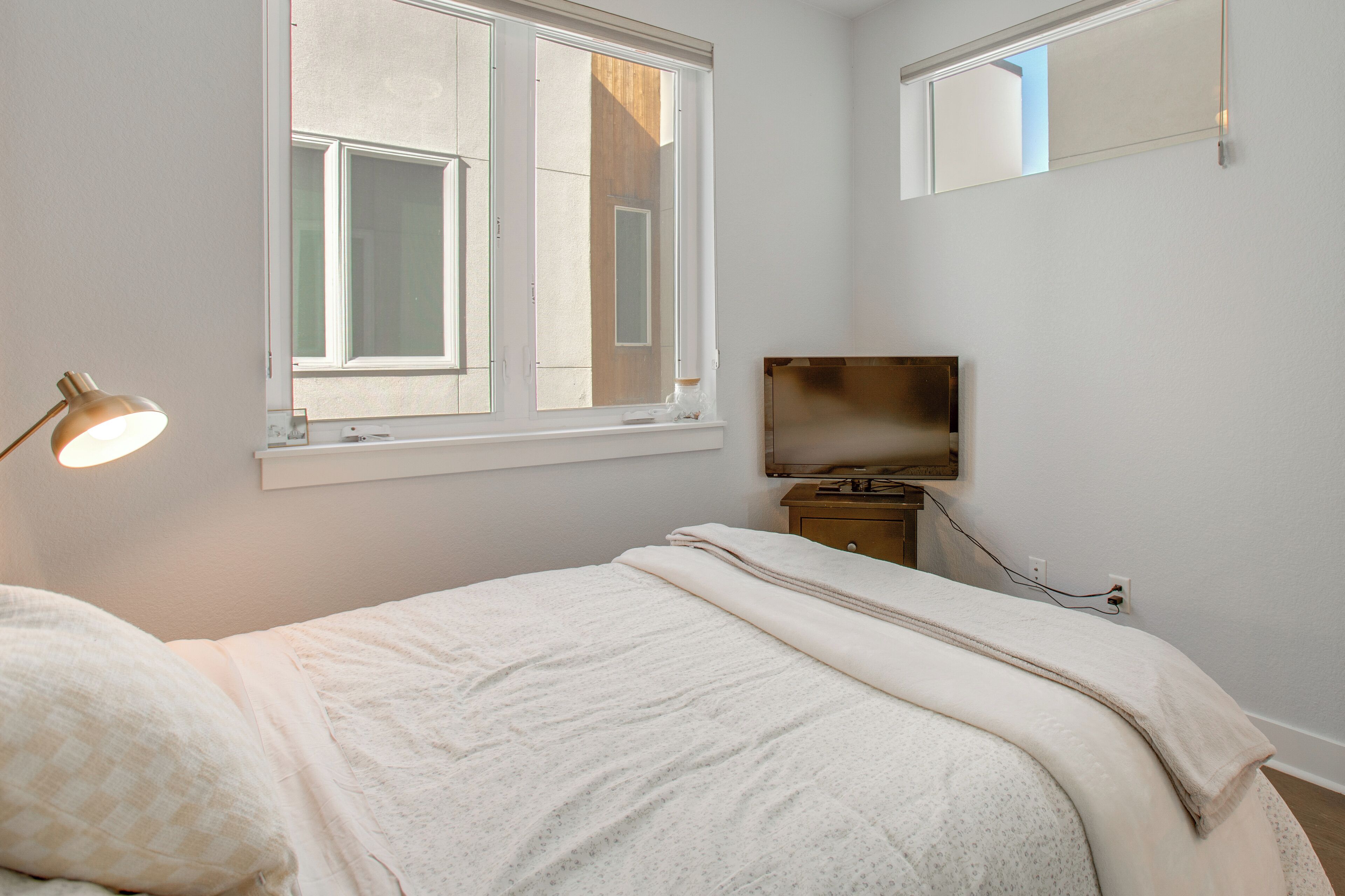 A bedroom with a bed, a bedside lamp, a TV, and a window.