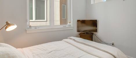 A bedroom with a bed, a bedside lamp, a TV, and a window.