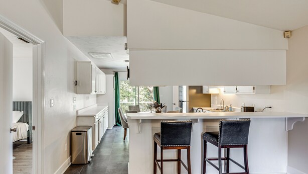 A modern kitchen with a central island, two bar stools, and a view into the adjacent bedroom. - 2 Mi to FSU: Pet-Friendly Retreat w/ Private Yard (Tallahassee)