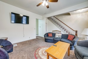 A living room with a flat-screen TV, a ceiling fan, a staircase, and a blue sofa. - Walk to Old Town Ottawa! Starved Rock Country Home (Ottawa)