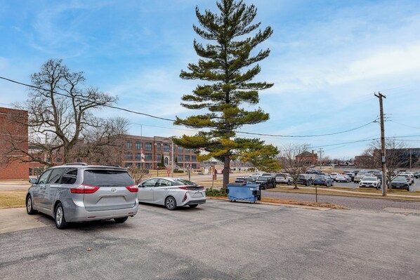 A parking lot with several cars, a large pine tree, and a brick building in the background. - Great Location! Walking Distance to So Much! (Ottawa)