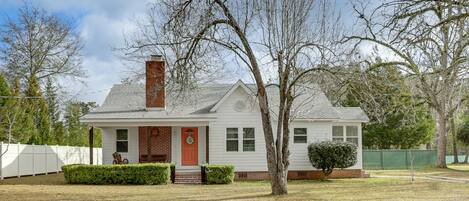 A single-story house with a brick chimney, white siding, and a red front door.
