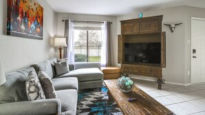 A living room with a sofa, a coffee table with decorative items, a television, and a painting on the wall.