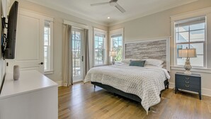 Quarto com cama, mesa de cabeceira, ventilador de teto e janela com cortinas.