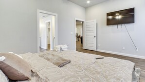 Une chambre à coucher avec un grand lit, un téléviseur à écran plat fixé au mur et une porte donnant sur une autre pièce.