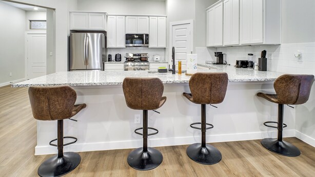 Une cuisine moderne avec des armoires blanches, des appareils en acier inoxydable et un coin bar équipé de tabourets.