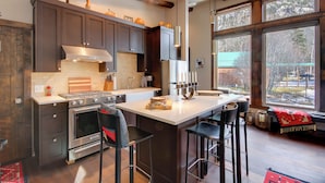 A modern kitchen with dark cabinets, a large island, and a view of the outdoors. - Boulder Dreams Guest House w/ Fire Pit! (Mc Leod)