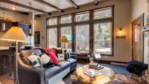 A modern living room with a leather sofa, a coffee table, and large windows offering a view of the outdoors. - Boulder Dreams Guest House w/ Fire Pit! (Mc Leod)