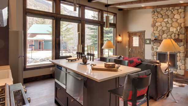 A modern kitchen with a large island, stone fireplace, and large windows offering a view of the outdoors. - Boulder Dreams Guest House w/ Fire Pit! (Mc Leod)