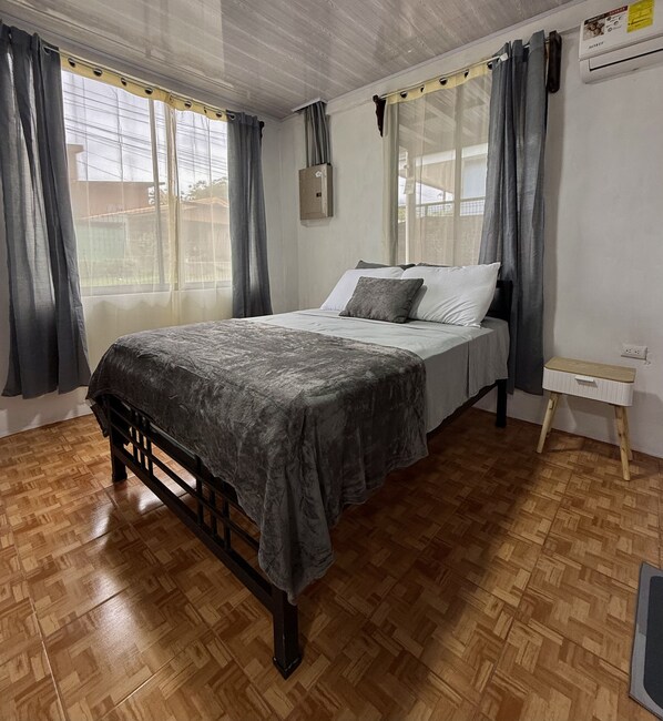 Une chambre à coucher avec un lit, un plancher en bois et une fenêtre avec des rideaux.