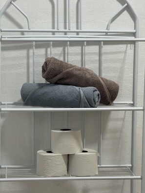 A white metal shelf unit with towels and toilet paper. - Apartamento Lapas  (La Fortuna)