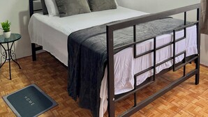 A bedroom with a bed, a small table with a plant, a window with curtains, and a radiator. - Apartamento Lapas  (La Fortuna)