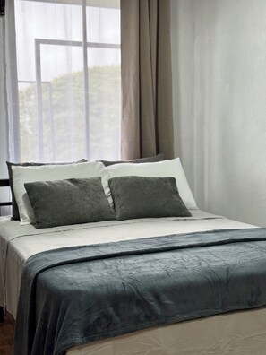A bed with a dark grey bedspread and pillows, a window with curtains, and a view of greenery outside. - Apartamento Lapas  (La Fortuna)