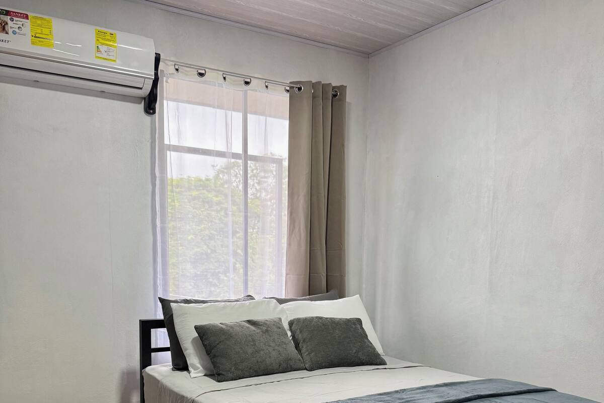 A bedroom with a bed, a bedside table, a window with curtains, and a radiator.