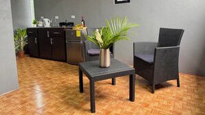 A room with a kitchen area, a dining table with chairs, and a potted plant. - Apartamento Lapas  (La Fortuna)