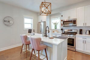 A modern kitchen with white cabinetry, stainless steel appliances, a central island with bar stools, and a decorative ceiling light. - Near Freeways! Centrally Located Denver Retreat (Denver)