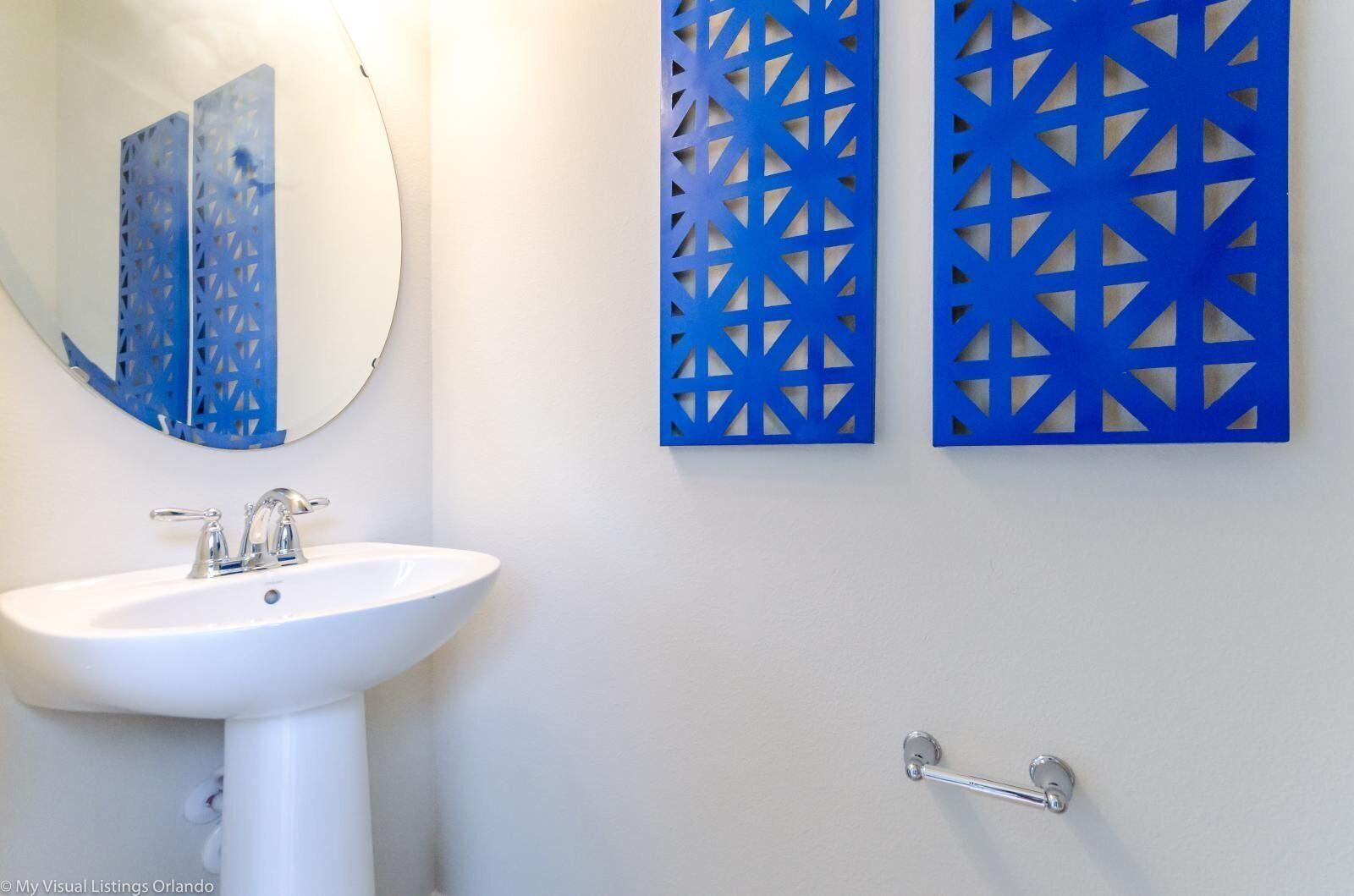 A bathroom with a white sink, a mirror, and two blue decorative panels on the wall.
