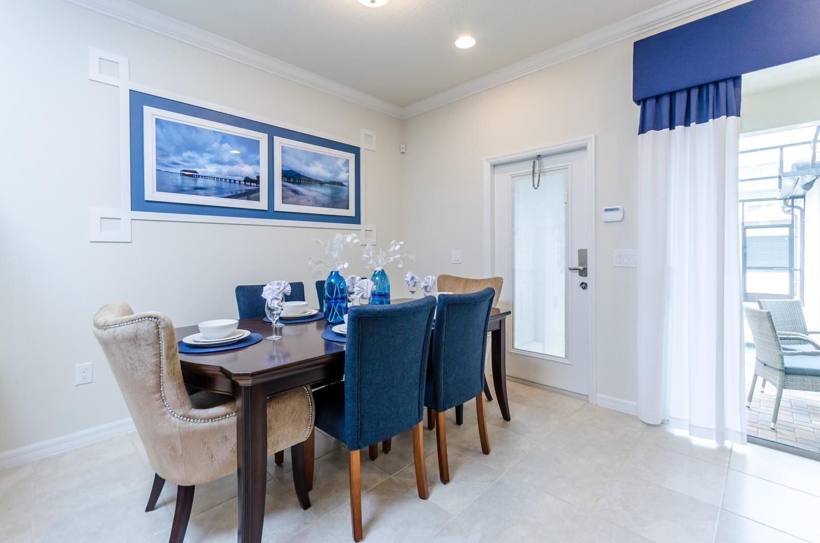 A dining area with a dark wooden table, blue chairs, and two framed pictures on the wall.
