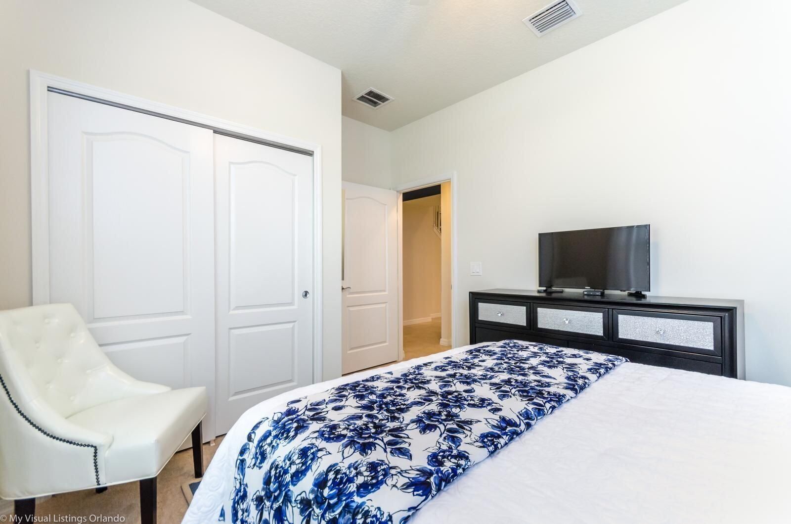 Een hotelkamer met een bed, een televisie op een dressoir, een witte stoel en twee witte deuren.