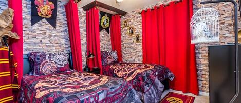 Une chambre avec deux lits, des rideaux rouges, un ventilateur de plafond, un mur en pierre et les armoiries de Poudlard.