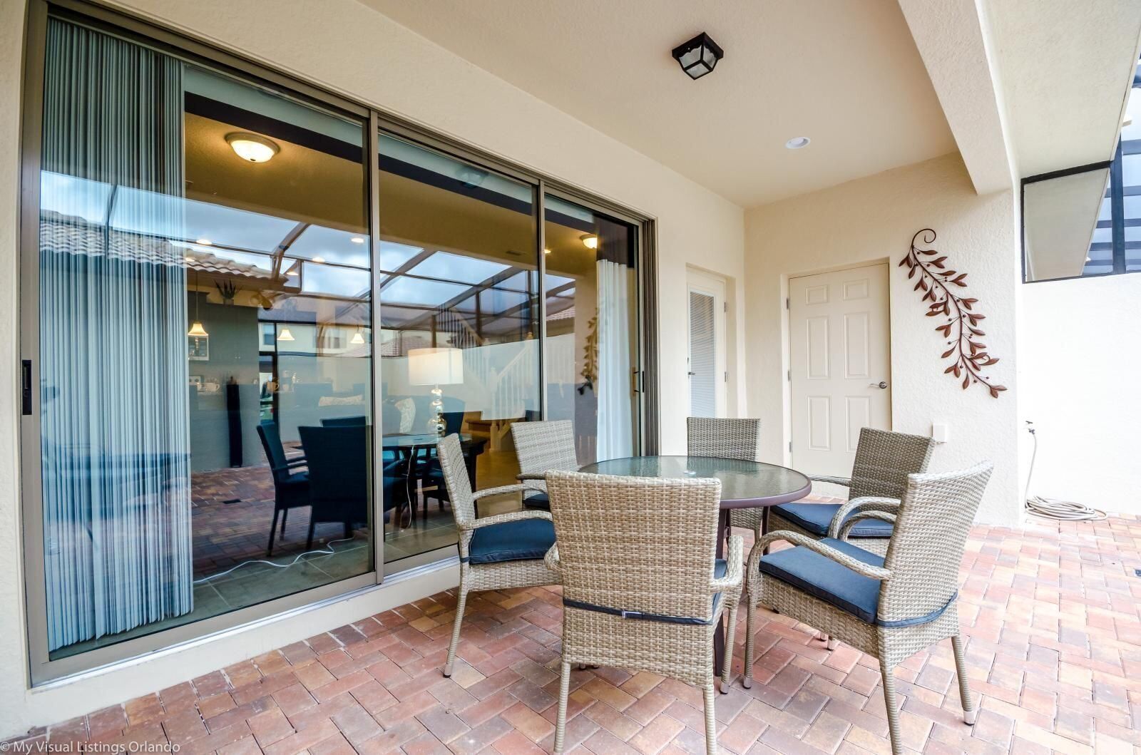 A patio with a glass door leading to an indoor dining area, wicker chairs, and a brick floor.