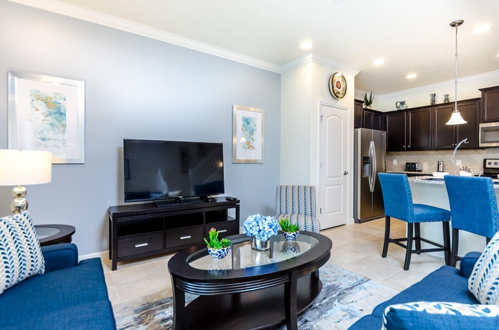 A modern living room with a flat-screen TV, a glass coffee table, and blue sofas.