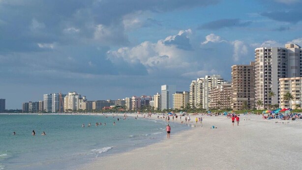 Ein Strand mit einer Stadtansicht im Hintergrund, darunter Hochhäuser und ein klarer Himmel.