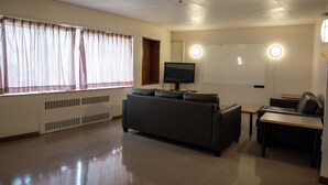 Una habitación con un ventanal grande, un televisor de pantalla plana, un sofá, una mesita y una pizarra.