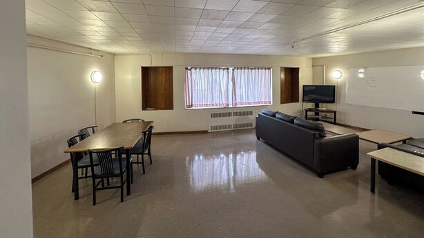 Una habitación con una mesa de madera, cuatro sillas, un sofá, un televisor y una ventana con cortinas.