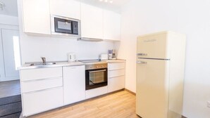 A modern kitchen with white cabinetry, a built-in oven, a microwave, and a cream-colored refrigerator. - Ferienresidenz Hinterzarten FEWO H4 (Hinterzarten)
