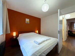 A neatly made bed with white linens and towels, a bedside lamp, and a framed picture on the wall. - Cosy 1BR Flat in East London (London)
