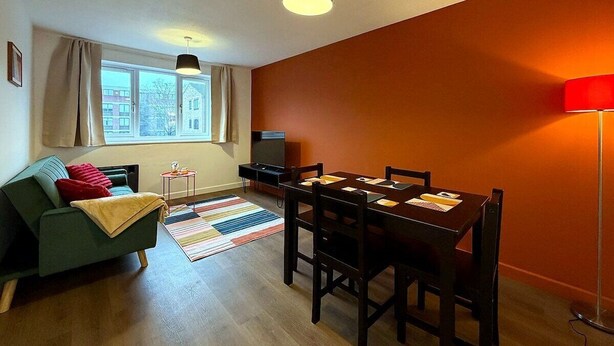 A compact living space with a sofa, dining table, and chairs, a television, and a window with curtains. - Cosy 1BR Flat in East London (London)
