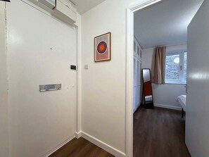 A hallway leading to a bedroom with a window, a door, and a wall-mounted picture. - Cosy 1BR Flat in East London (London)