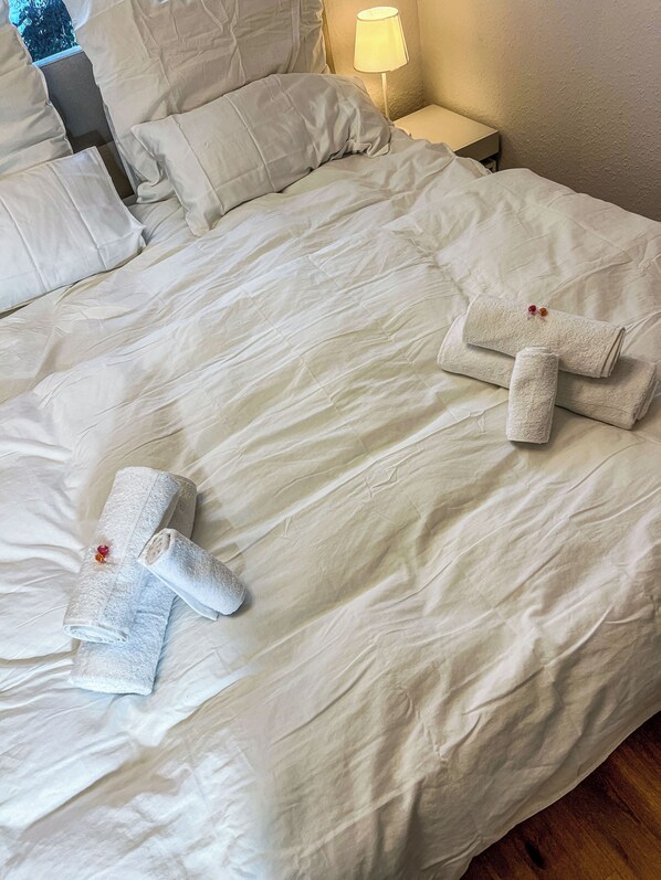 Un lit bien fait, avec des draps blancs et deux serviettes pliées en forme de croix, posées sur le lit.