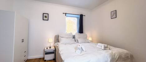 A bedroom with a bed, bedside tables, a window with curtains, and a door.