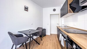 A compact kitchen with a dining area, featuring a modern stove, a sink, and a small table with chairs. - Modern & Cozy Apartment | Central Magdeburg | (Magdeburg)