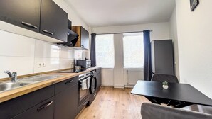 A compact kitchen with a sink, stove, microwave, and oven. There is a dining table with a chair and a small plant. - Modern & Cozy Apartment | Central Magdeburg | (Magdeburg)