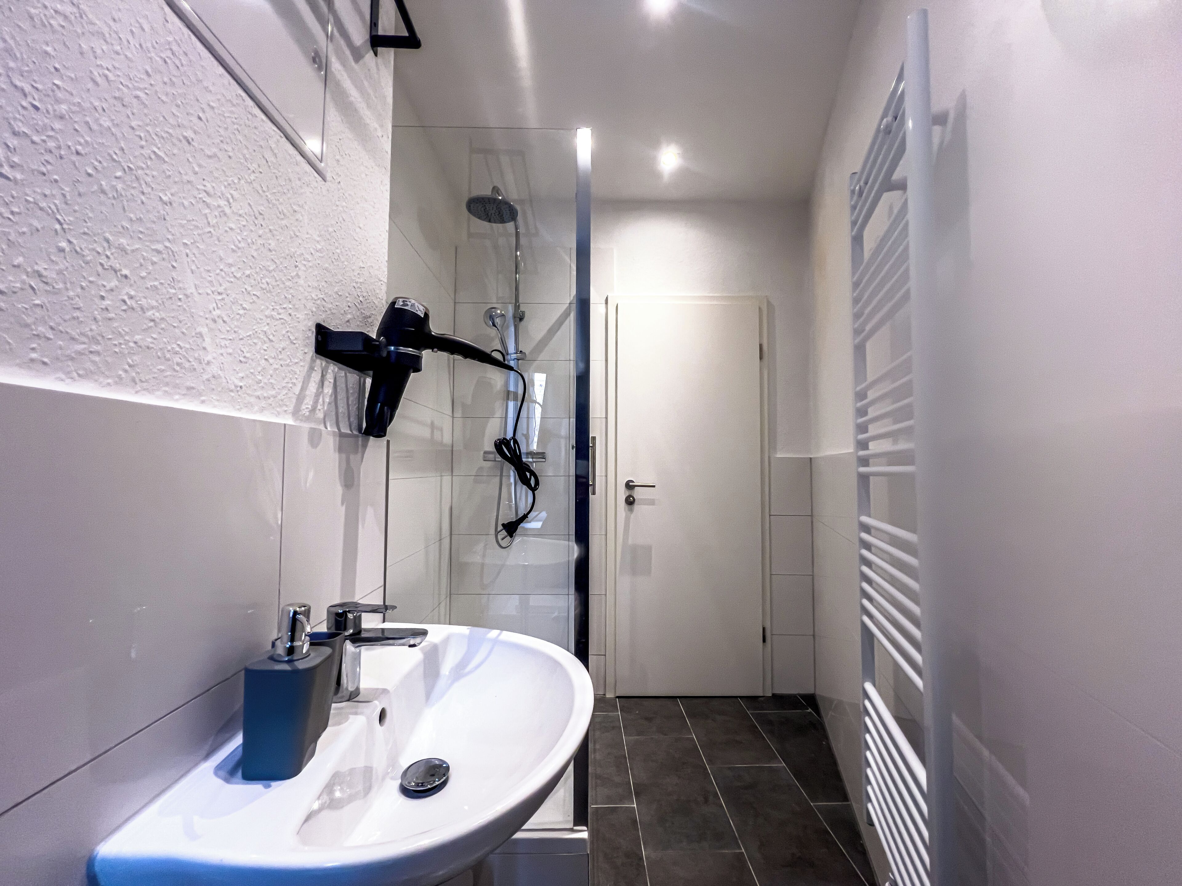 Een moderne badkamer met een wit wastafelmeubel, een handdouche en een douchecabine met glazen wanden.