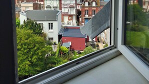 En utsikt över en kuststad från ett fönster, med traditionell arkitektur i förgrunden, en klar himmel och havet i bakgrunden.