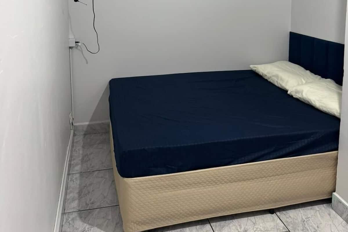 A small, neatly arranged bedroom with a single bed, a television mounted on the wall, and a power outlet on the wall.