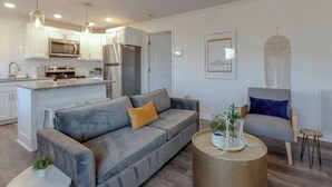 Un salon moderne avec un canapé gris, une table basse ronde et un fauteuil agrémenté d’un coussin bleu.