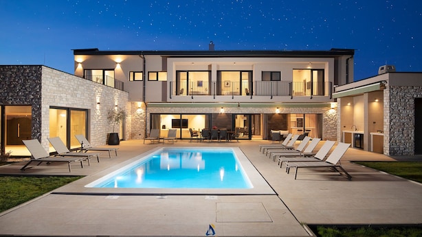 Une maison moderne à deux étages, dotée d’une piscine, d’un espace extérieur aménagé et d’une façade en pierre.
