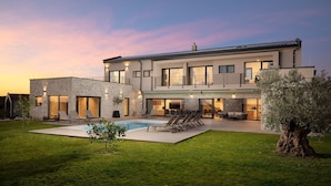 Une maison moderne à deux étages, dotée d’une façade en pierre, d’une piscine et d’une pelouse bien entretenue.
