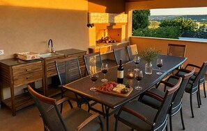 Un espace repas avec une longue table, des chaises, une bouteille de vin, des verres et une planche de charcuterie.