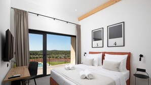 Habitación de hotel con cama, escritorio, silla, televisión y vista a una piscina y paisaje.
