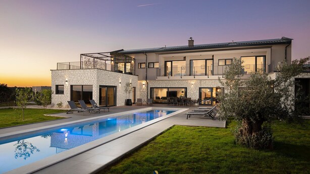 Una casa moderna de dos pisos con piscina, mobiliario exterior y un césped bien cuidado.