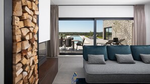 Una sala moderna con pared de piedra, un sofá con cojines y vistas a una piscina y zona de estar al aire libre.