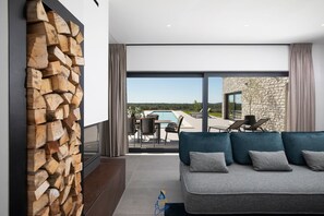 Uma sala de estar moderna com parede de pedra, um sofá com almofadas e vista para uma piscina e área de estar externa.