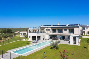 Una casa moderna de dos pisos con piscina, paneles solares y un césped bien cuidado.