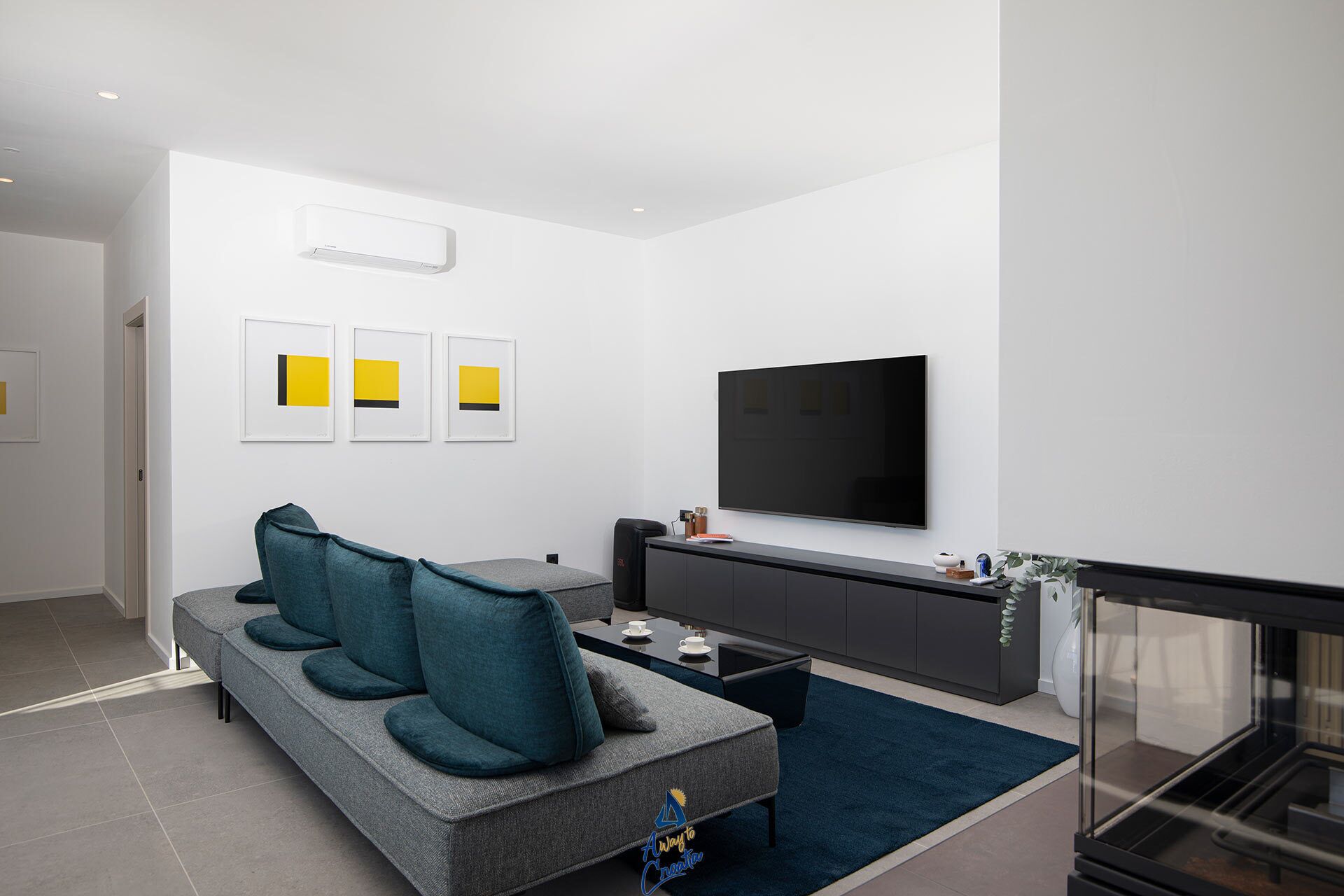 A modern living room with a grey sofa, teal cushions, a flat-screen TV, and a small coffee table.